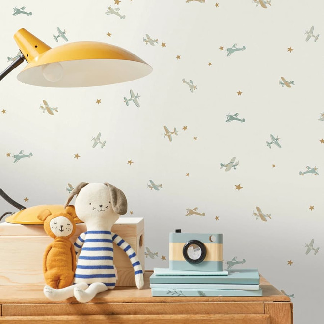 Papel de parede infantil com avionetas e estrelas aplicado em quarto de criança com decoração em madeira e tons naturais.